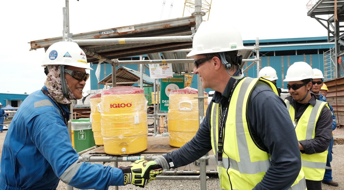 Bechtel President and COO Craig Albert and a fellow Bechtel team member in safety gear shaking hands on a project site. 