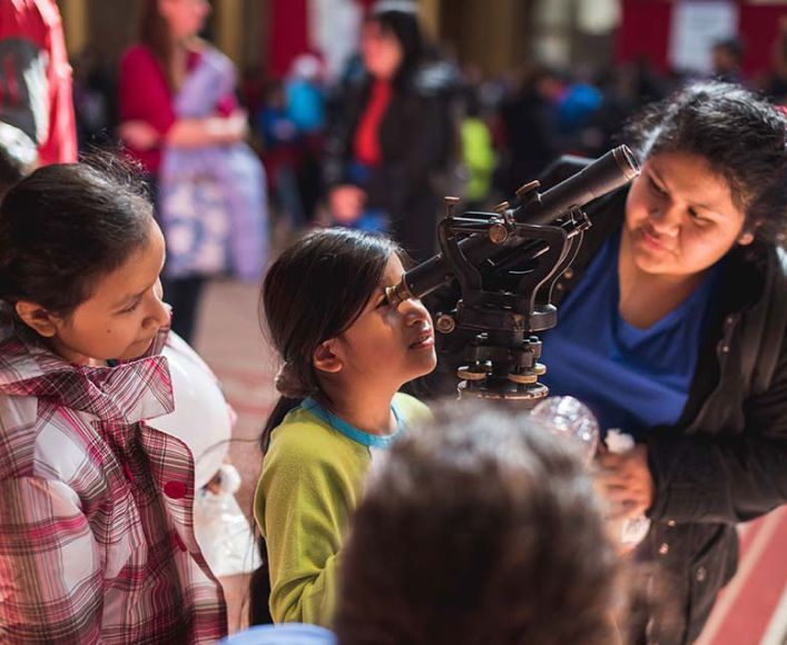 A young girl looking into a telescope at Noche de Ciencias.