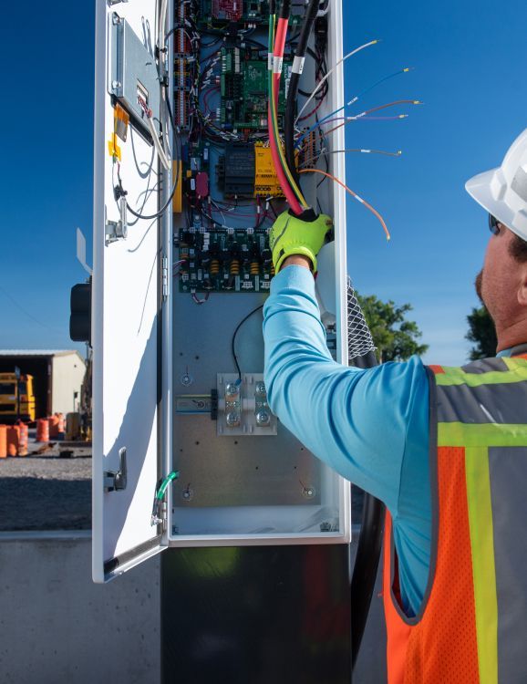 Person wearing safety gear adjusting wiring inside an electric vehicle charging station.