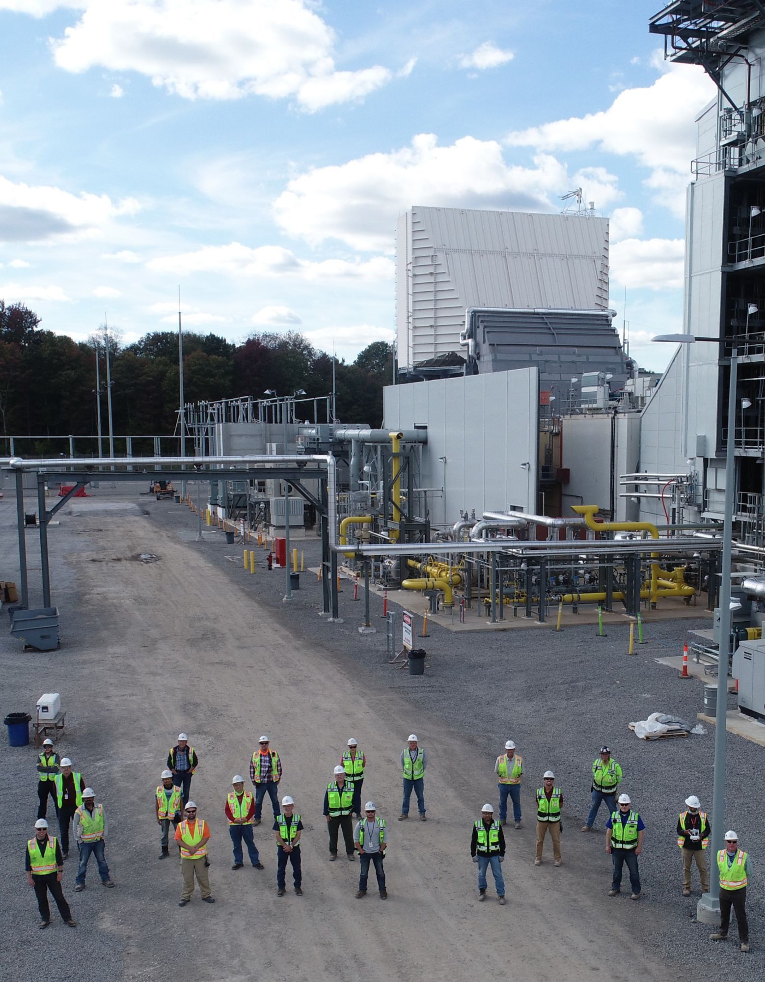 Aerial view of a group standing in front of a project site wearing hard hats and safety vests.