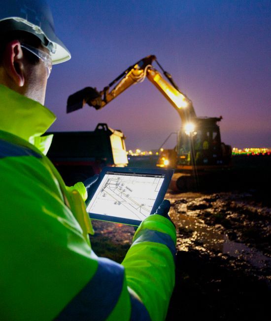 Person in safety gear using a tablet on a project site.