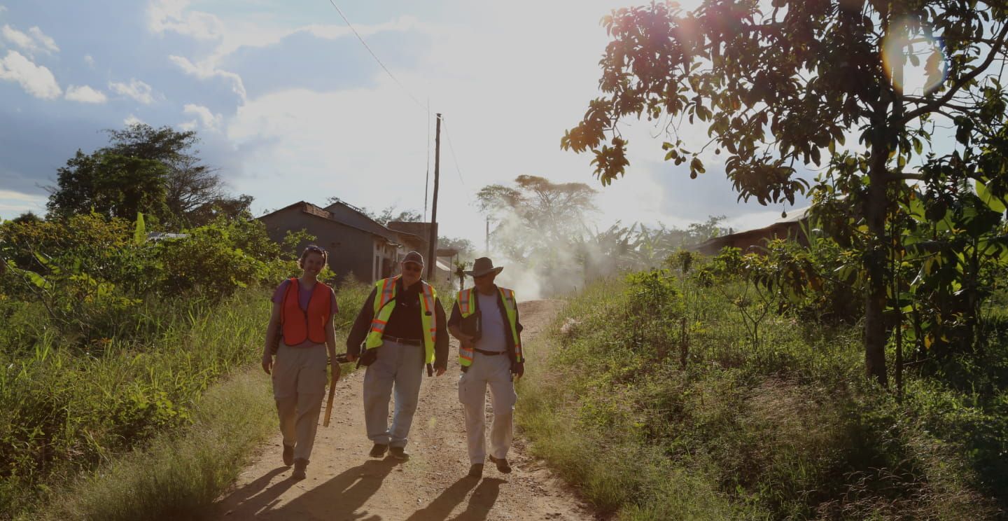 Three people wearing safety vests and walking along a dirt road.