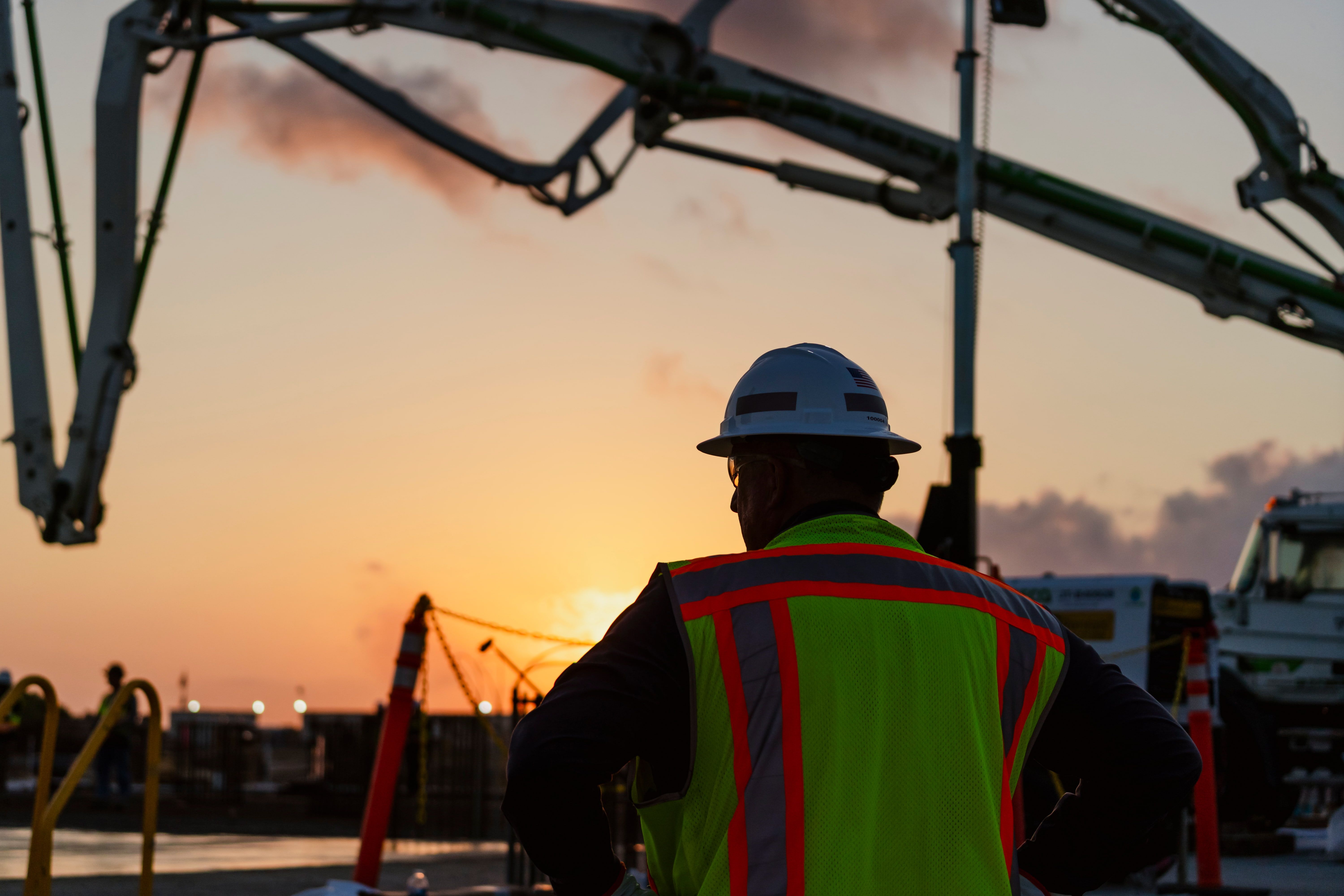 Worker in a high-visibility jacket facing the sunset on a construction site.