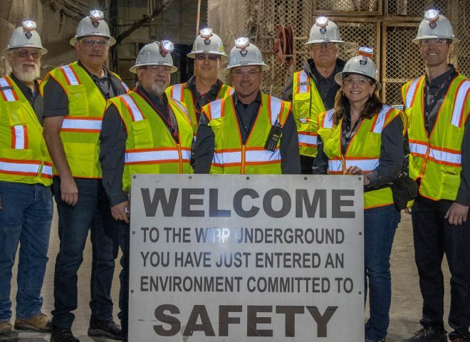 A group of Bechtel team members wearing safety gear in front of a Welcome sign that acknowledges a commitment to safety.