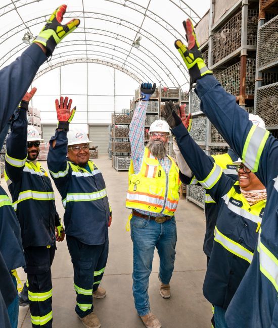 Group of Bechtel team members in safety gear raising hands as part of a team huddle.