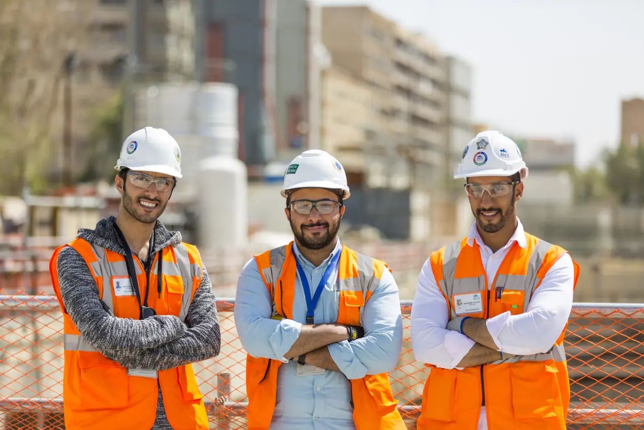 Three smiling workers in safety gear in Riyadh.