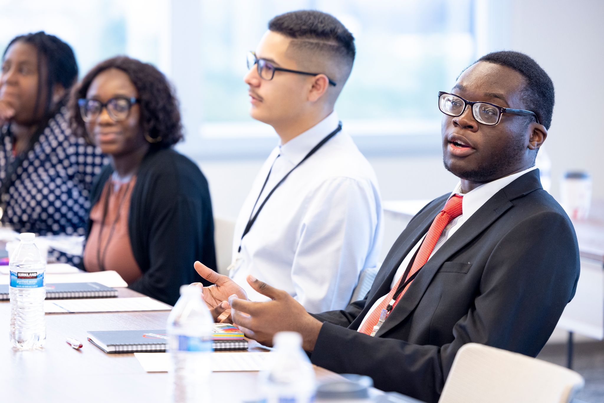 A young Black man speaking at a table alongside three other minority students.