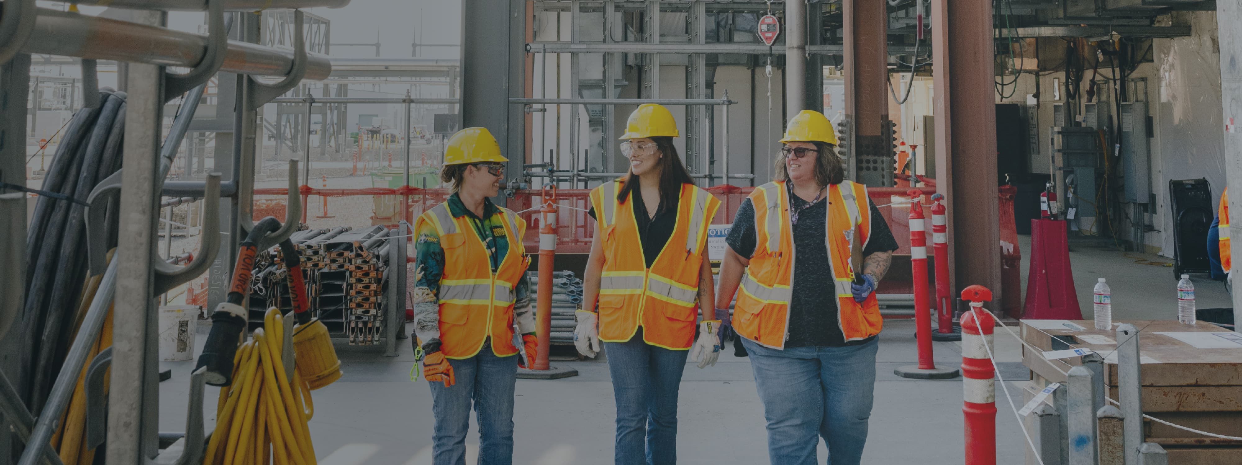 Three women in hard hats and safety vests on project site.