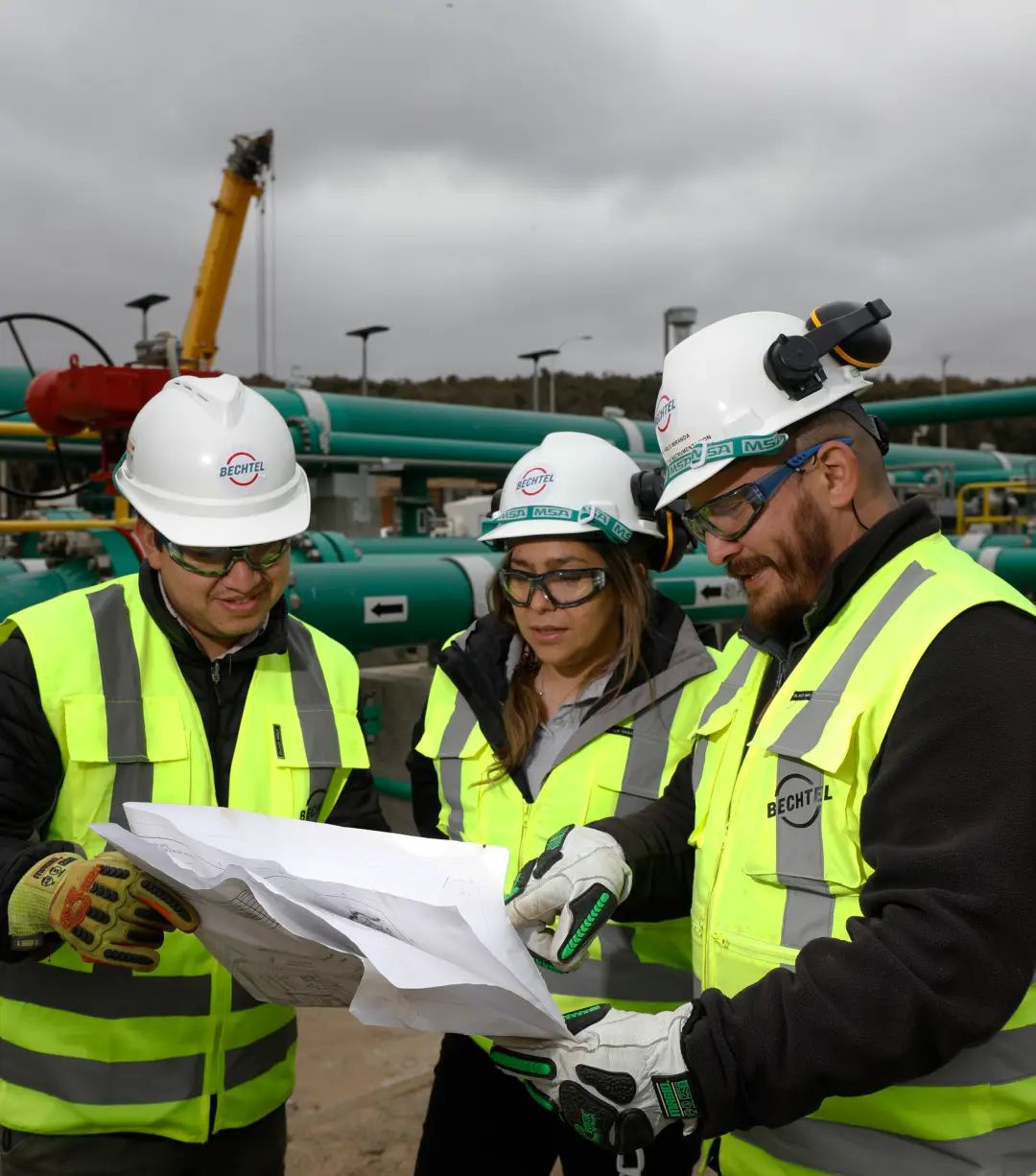 Three Bechtel team members in safety gear looking at a set of plans.