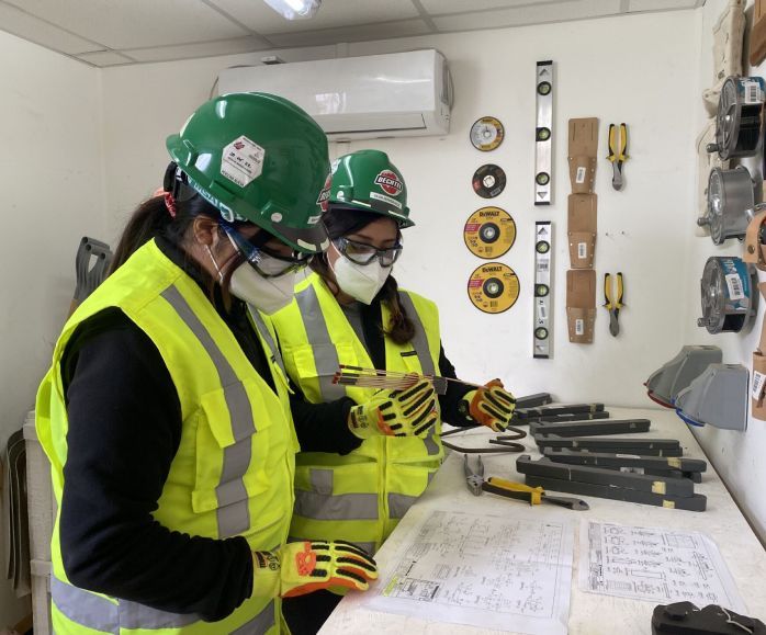 Two women wearing safety gear reviewing project plans.